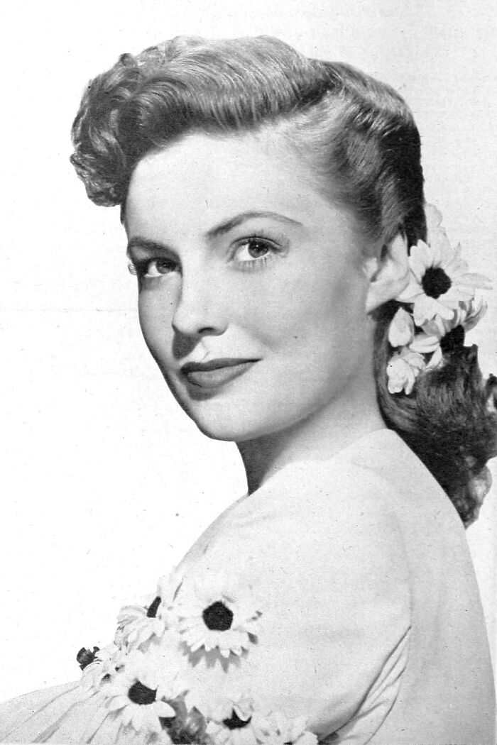 Black and white portrait of a glamorous 1940s icon with styled hair and flowers, embodying Hollywood elegance.