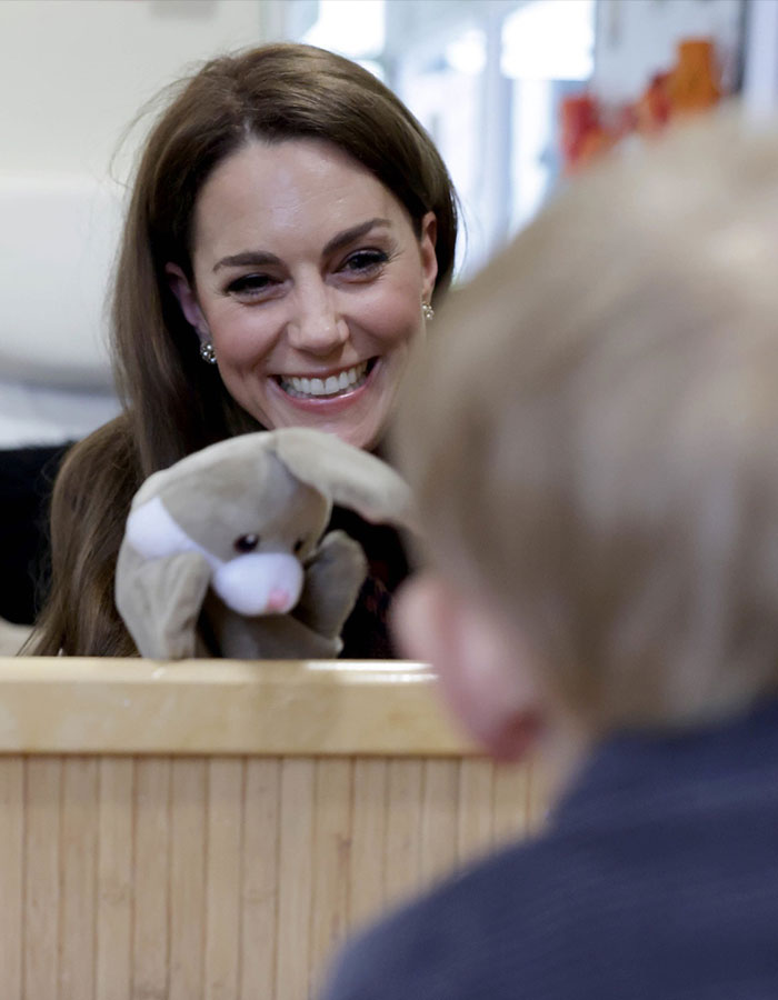 Kate Middleton smiling warmly at a child while holding a stuffed animal, related to Meghan Markle clash details.
