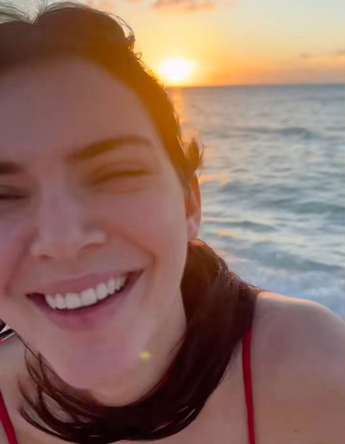 Smiling woman enjoying a sunset beach walk with ocean waves in the background, showcasing talent and carefree vibes.