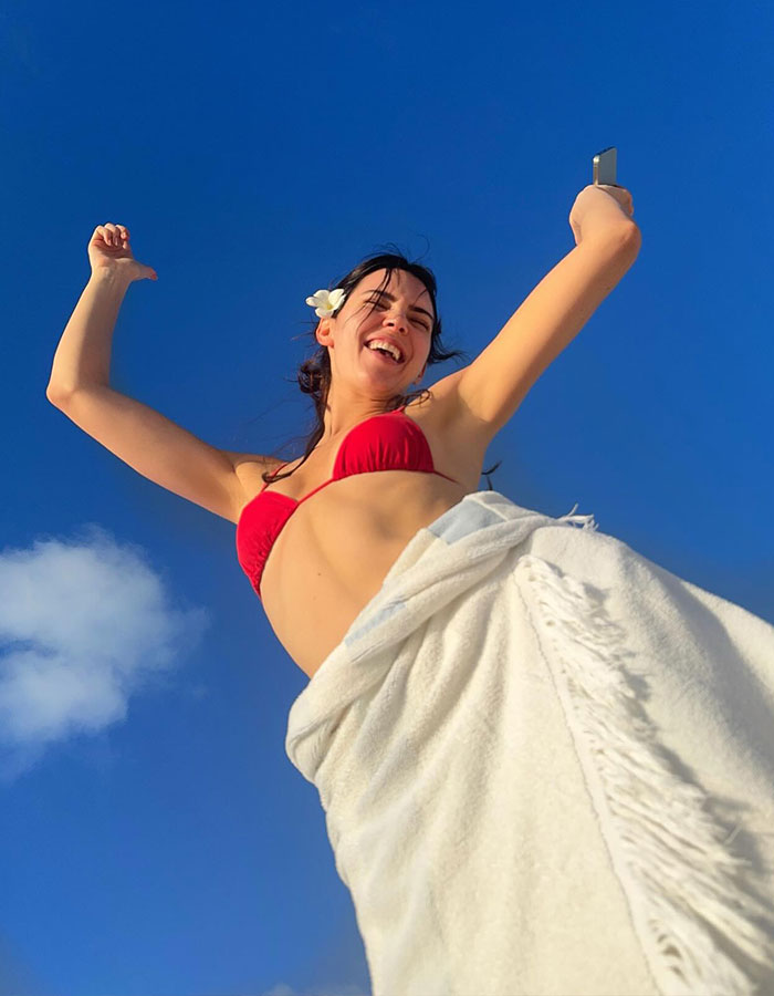 Young woman in a red bikini enjoying a joyful beach walk under a clear blue sky, capturing a lively moment outdoors.