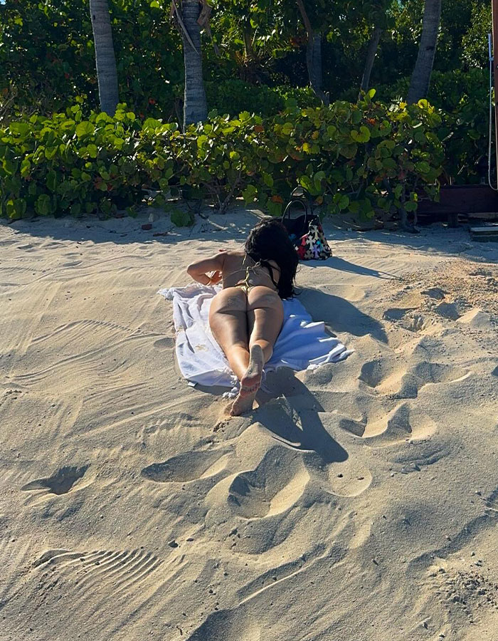 Woman in a revealing golden bikini lying on a beach towel, flaunting round butt with tropical greenery in the background Woman in a revealing golden bikini lying on a beach towel, flaunting round butt with tropical greenery in the background