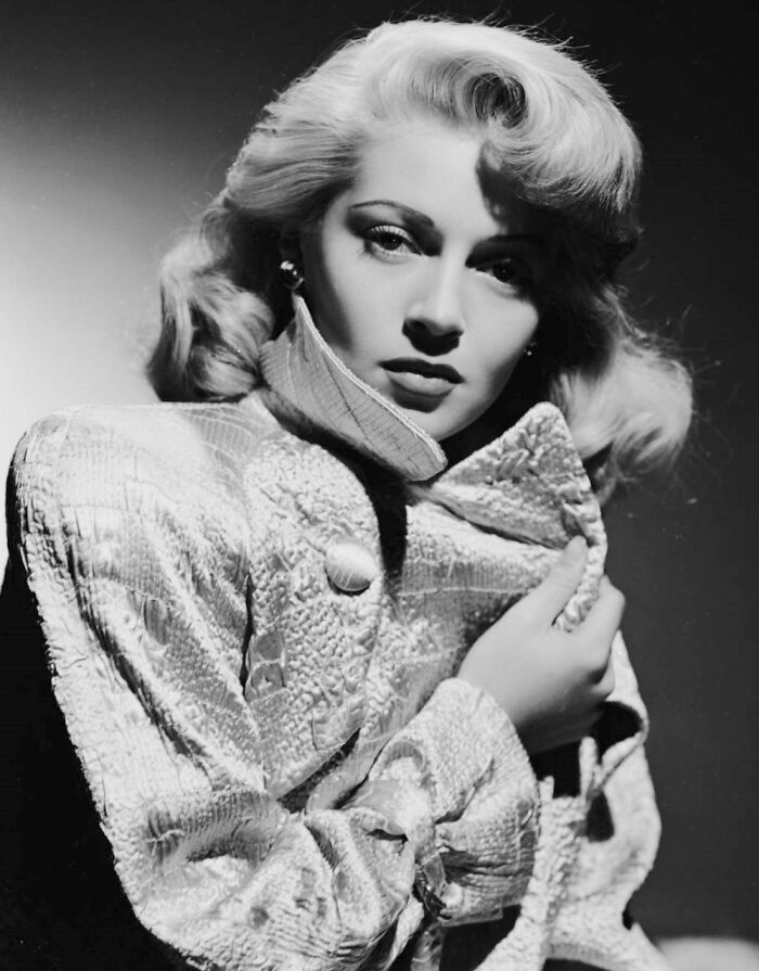 Glamorous 1940s icon in a textured coat posing dramatically in classic Hollywood black and white portrait.