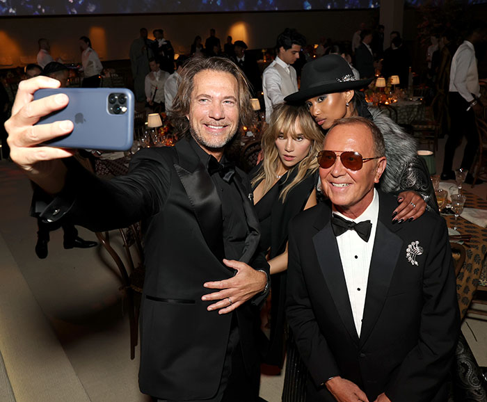 Celebs breaking Met Gala no phones rule, taking selfie inside event with formal attire and dimly lit background.