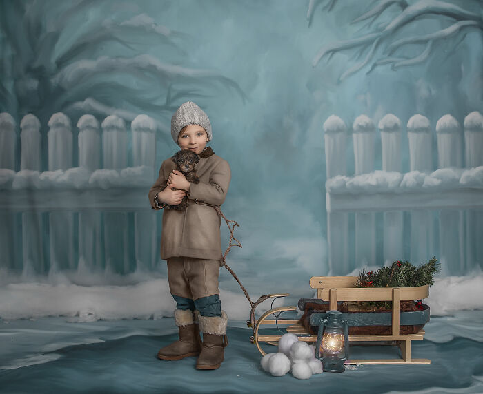 Child in winter clothes holding a puppy, standing next to a wooden sled in a snowy whimsical portrait capturing magical bond.
