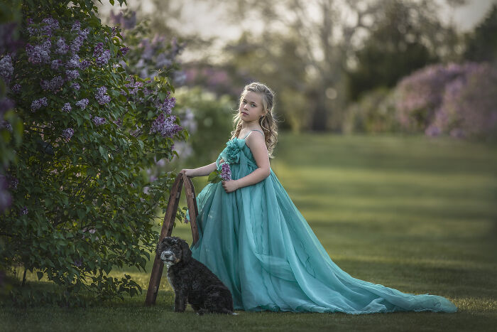Young girl in a whimsical turquoise dress with a small black dog, capturing the magical bond between children and animals outdoors.
