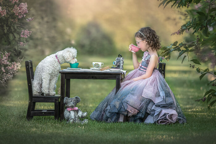 Young girl in a whimsical dress having a tea party with a white dog, capturing the magical bond between children and animals outdoors.