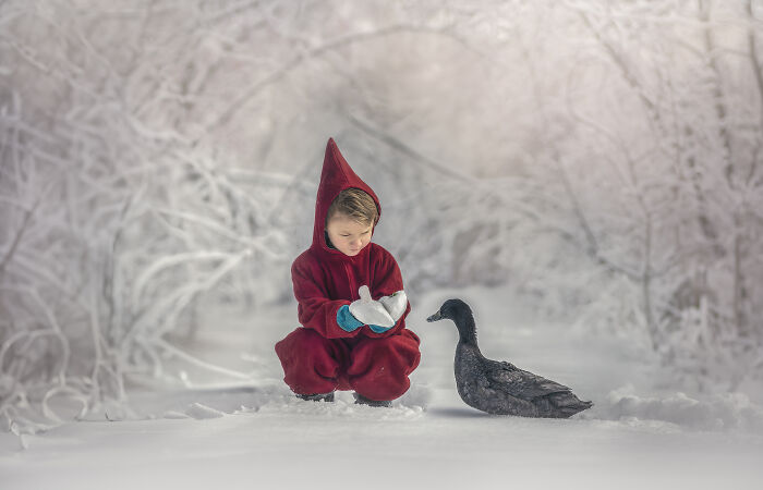 Child in red winter clothing gently interacting with a duck, capturing the magical bond between children and animals in snow.