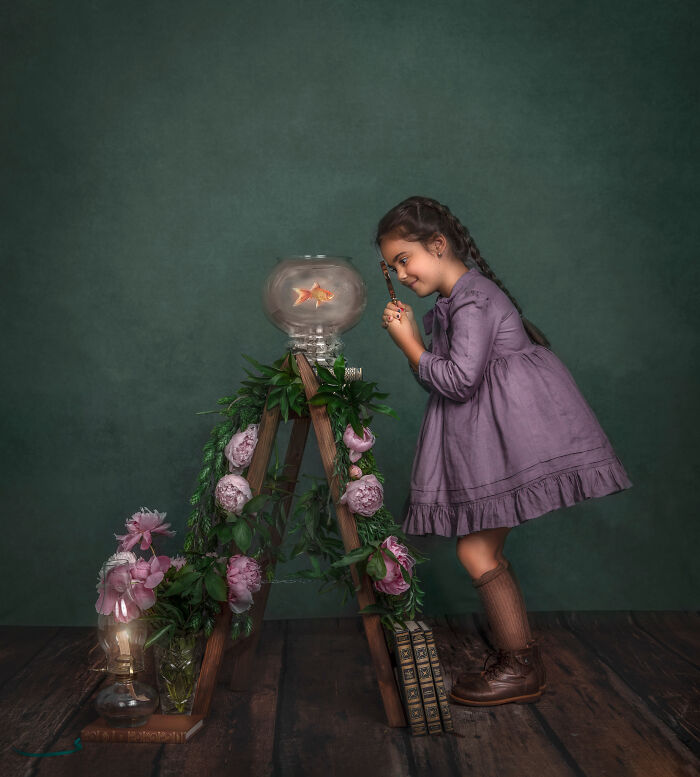 Young girl in a whimsical portrait closely observing a goldfish, capturing the magical bond between children and animals.