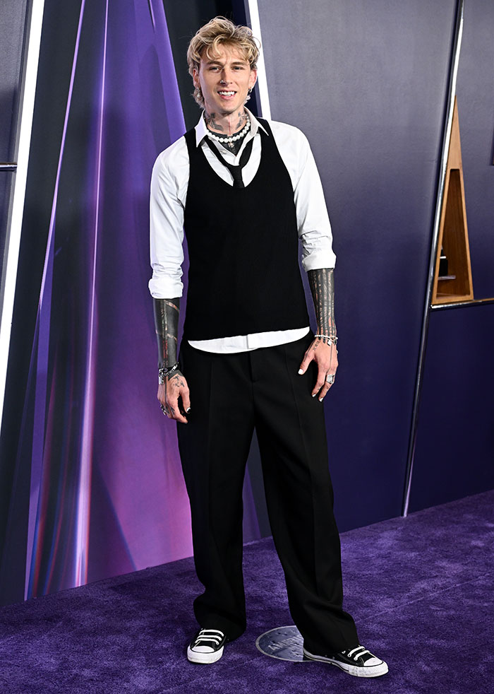 Young man with tattoos wearing a casual black and white outfit at an event highlighting worst dressed stars 2025 American Music Awards.