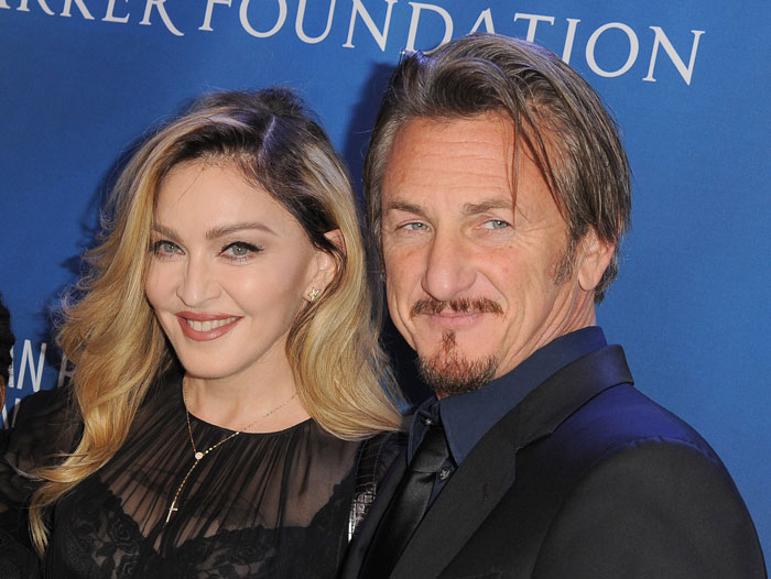 Sean Penn and Madonna posing together on a blue carpet backdrop with smiles and formal attire.