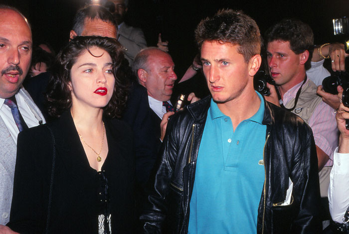 Sean Penn and Madonna walking together, surrounded by photographers at a public event, capturing a tense moment.