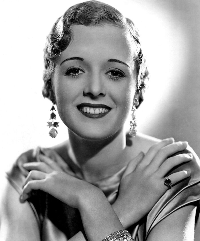 Black and white portrait of a glamorous 1940s icon smiling, showcasing classic Hollywood elegance and style.