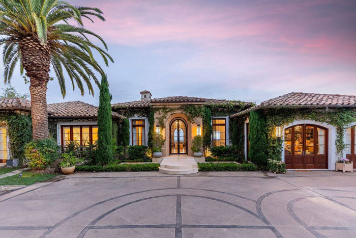 Luxury Montecito home with Mediterranean design, lush greenery, and a vibrant sunset sky in a controlled image setting.