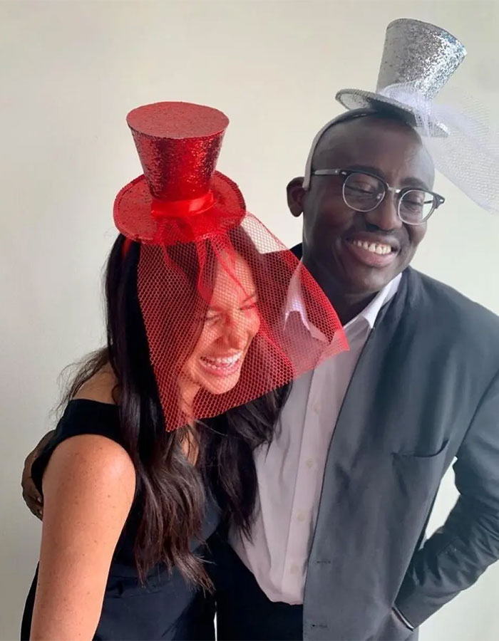 Two people smiling and wearing glittery red and silver hats with veils, illustrating Meghan Markle Vogue cover diva story.