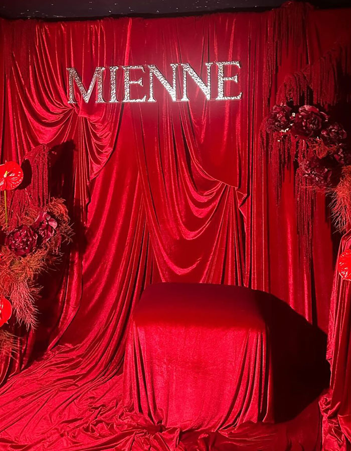 Red velvet draped backdrop with MIENNE sign and floral decorations at a skincare launch event setting.