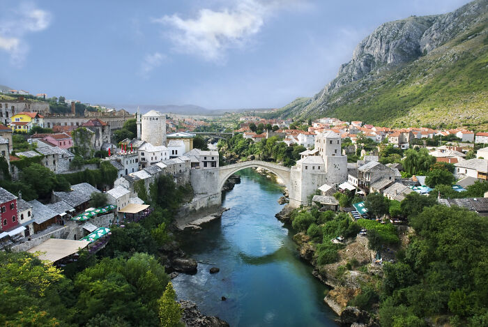 Historic stone bridge over river in a scenic town surrounded by mountains, a hidden UNESCO gem in Europe.