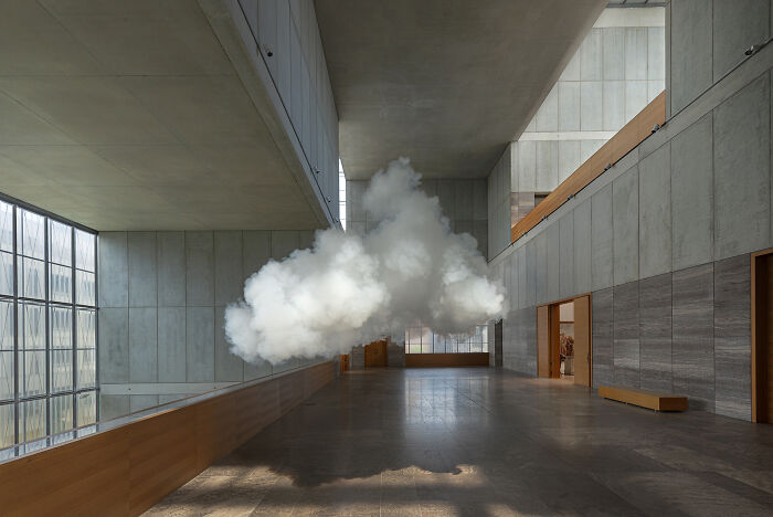Realistic cloud made of smoke and water vapor installation floating inside a modern indoor space with concrete walls.