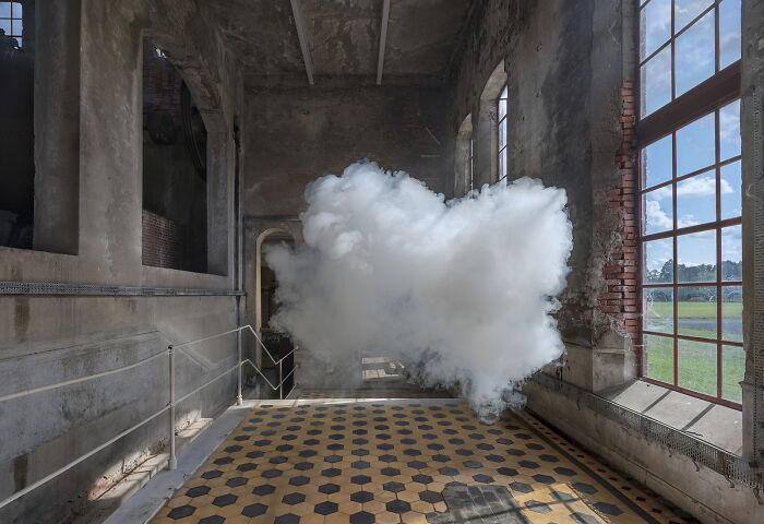 Realistic cloud made from smoke and water vapor floating inside an old industrial indoor space near large windows.