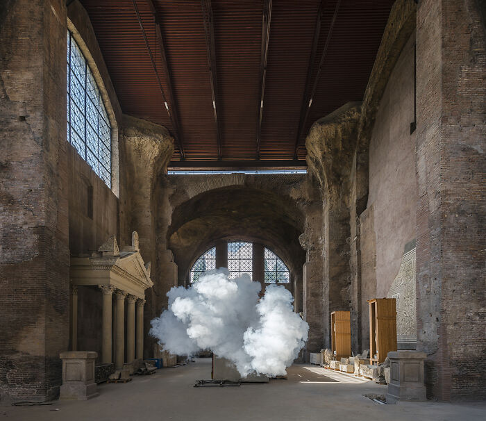 Realistic clouds created with smoke and water vapor forming an art installation inside a large indoor space.