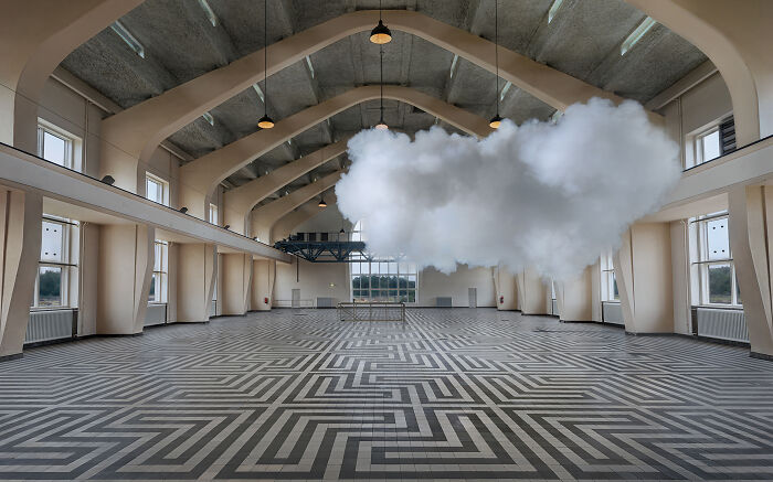 Realistic cloud created with smoke and water vapor suspended inside a large indoor space with patterned flooring.