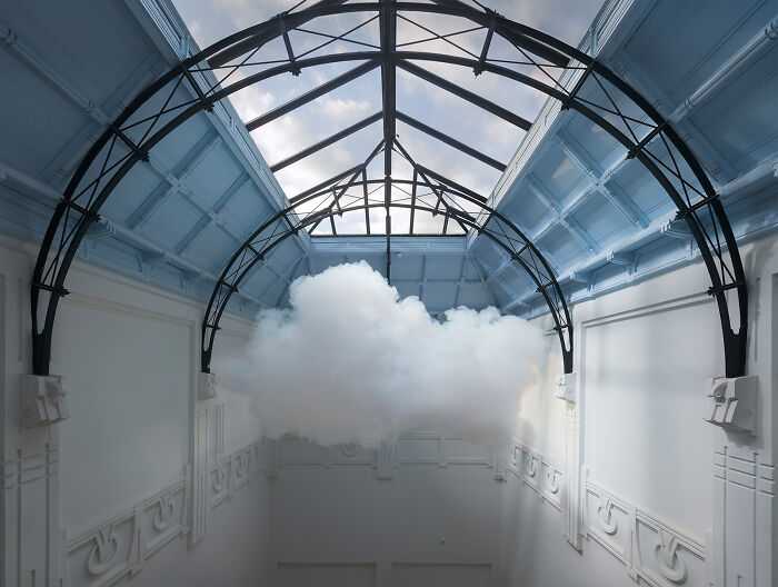 Realistic cloud created with smoke and water vapor installation inside an indoor space with glass ceiling and metal framework.