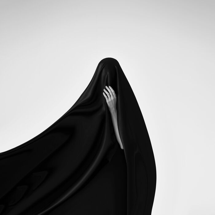 Person partially hidden under flowing black fabric in minimalist studio setting showcasing power of a single frame photography.