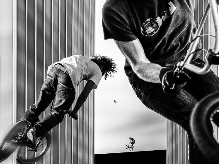 Black and white action shot of BMX riders performing tricks between tall buildings, capturing the power of a single frame.