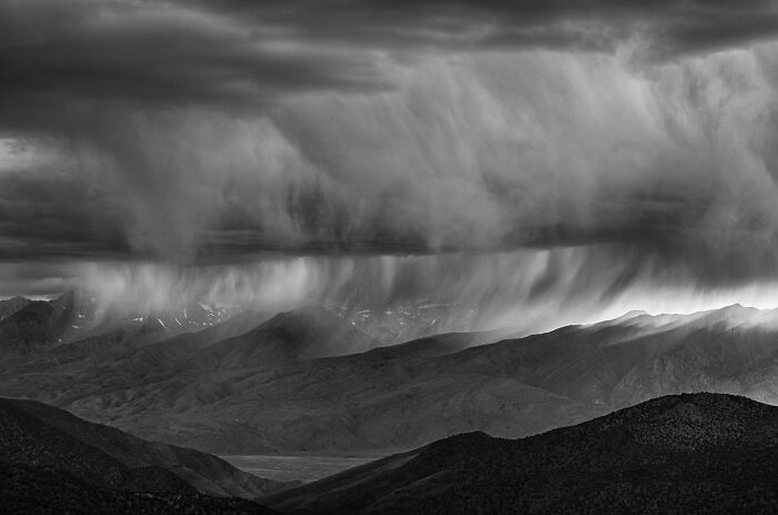 Dramatic black and white landscape of mountains with rain clouds captured in the 2025 One Shot Photo Contest winners.