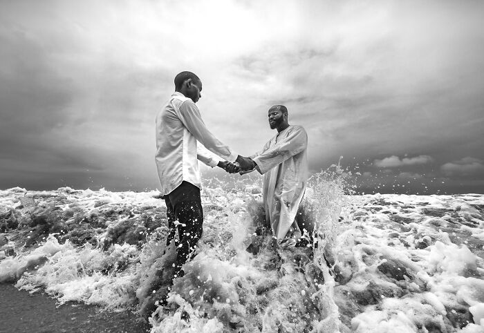 Two men standing in ocean waves shaking hands, capturing a powerful moment from the 2025 One Shot photo contest winners.
