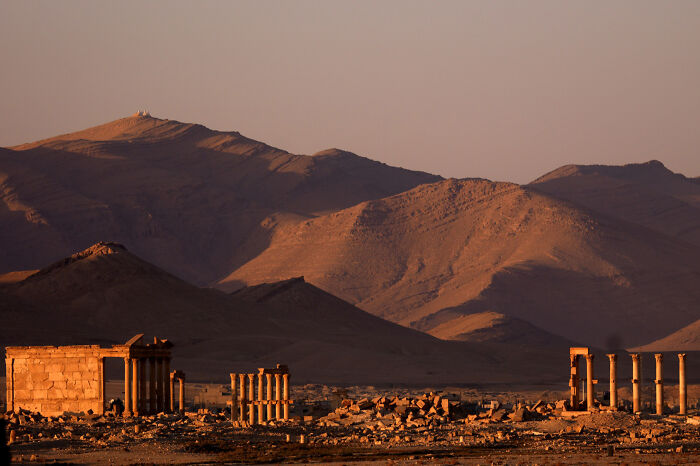 Ancient UNESCO treasures with stone ruins and columns set against mountains bathed in warm sunset light.