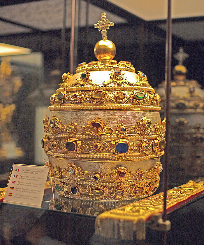 Ornate golden papal tiara with jewels displayed in a museum case, highlighting fascinating pope facts and history.