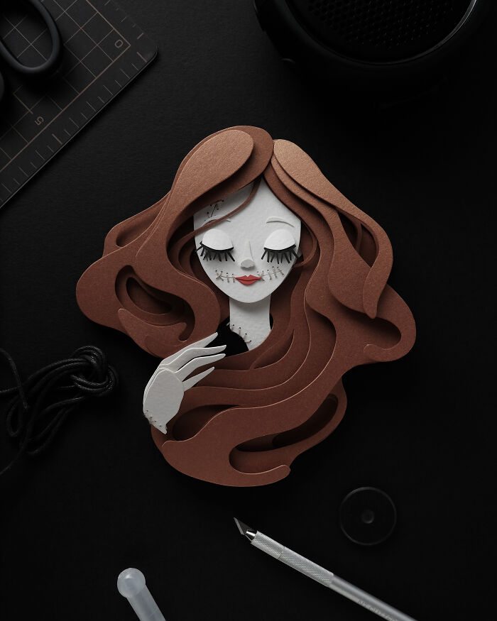 Intricate and colorful paper art depicting a stylized female face with flowing hair and delicate hand details on black background.