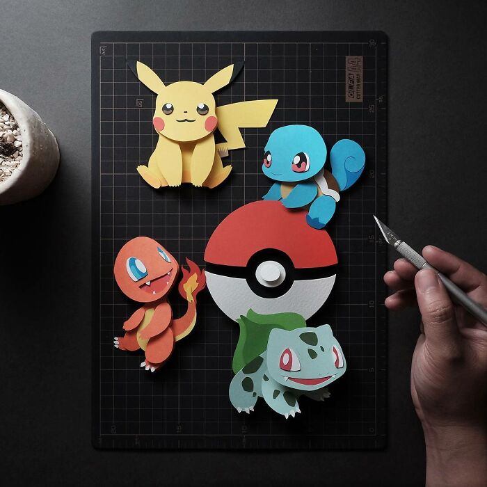 Colorful and intricate paper art featuring popular characters and a Pokeball crafted with detailed precision on a cutting mat.