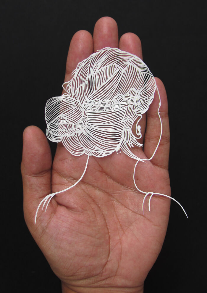 Hand holding intricate paper art silhouette of a woman’s head with braided hair, showcasing delicate paper art craftsmanship.