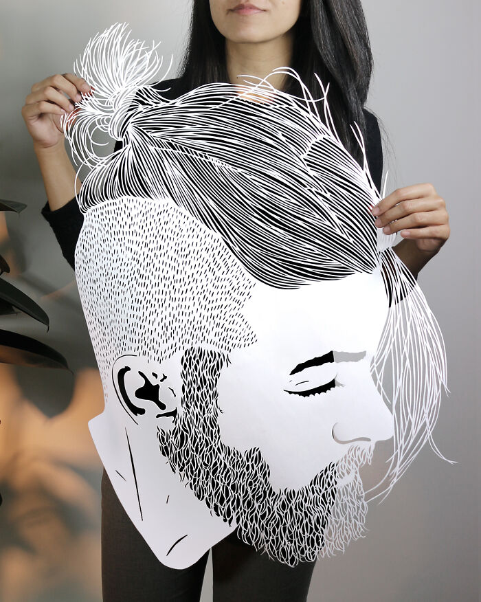 Woman holding intricate paper art portrait of a bearded man with detailed hair and beard, showcasing colorful paper art skills.