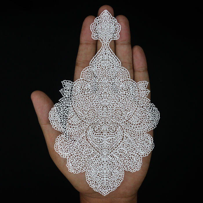 Hand holding intricate and delicate white paper art with detailed lace-like patterns against a black background.