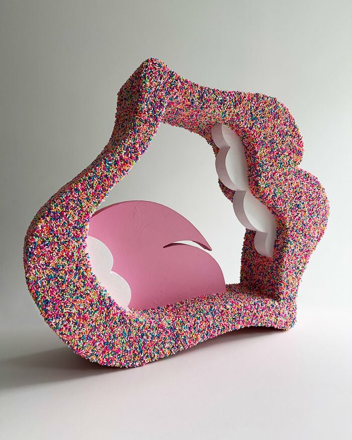 Abstract colorful artwork made by covering an irregular-shaped object in vibrant sprinkles with pink and white accents.