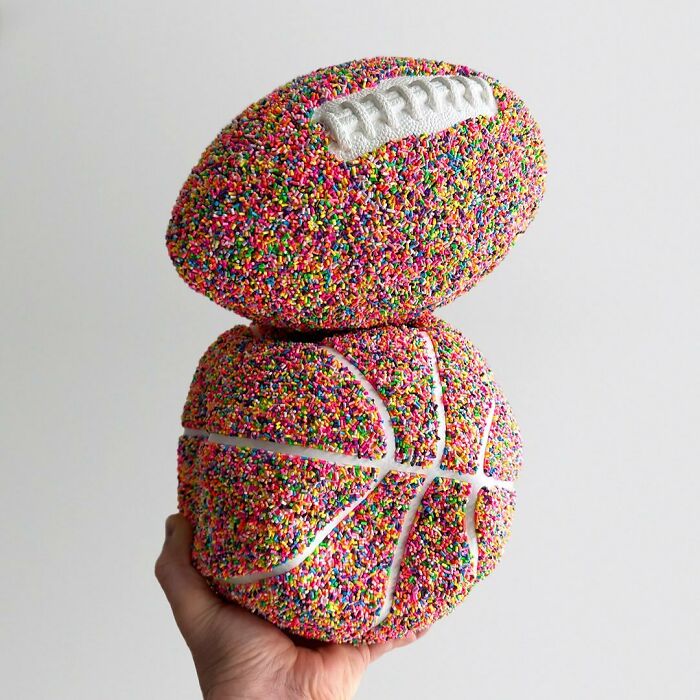 Hand holding basketball and football sculptures uniquely covered in colorful sprinkles as vibrant artwork.