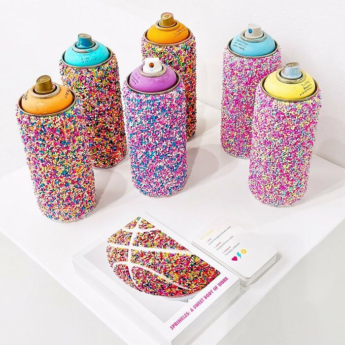 Six spray paint cans covered in colorful sprinkles displayed as unique artworks by Pepe Bratanov on a white surface.