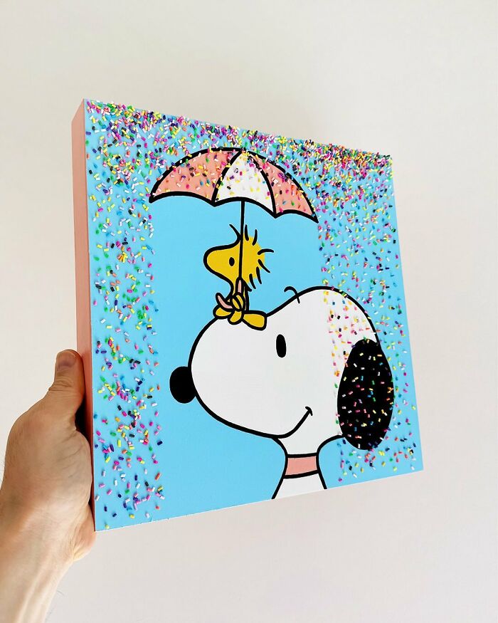 Hand holding a colorful artwork of a dog and bird covered in sprinkles, showcasing unique sprinkle art by Pepe Bratanov.