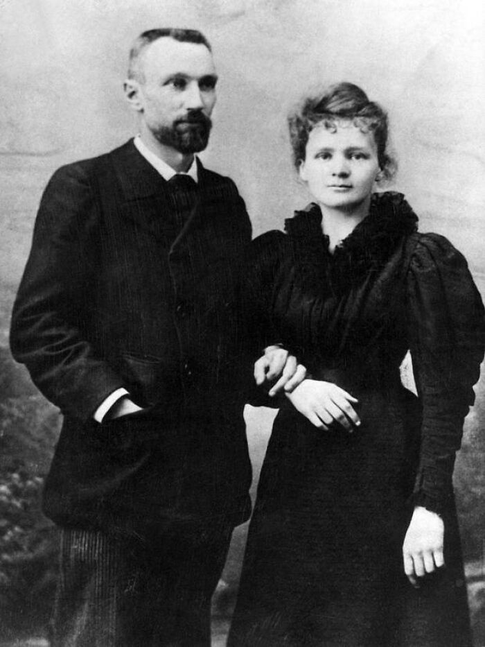 Black and white photo of Marie Curie and a man, both dressed in early 20th century formal clothing, posing together.