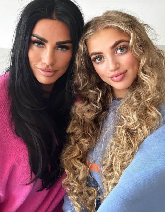 Princess Andre with long curly hair posing alongside a woman with straight black hair indoors, both smiling gently.