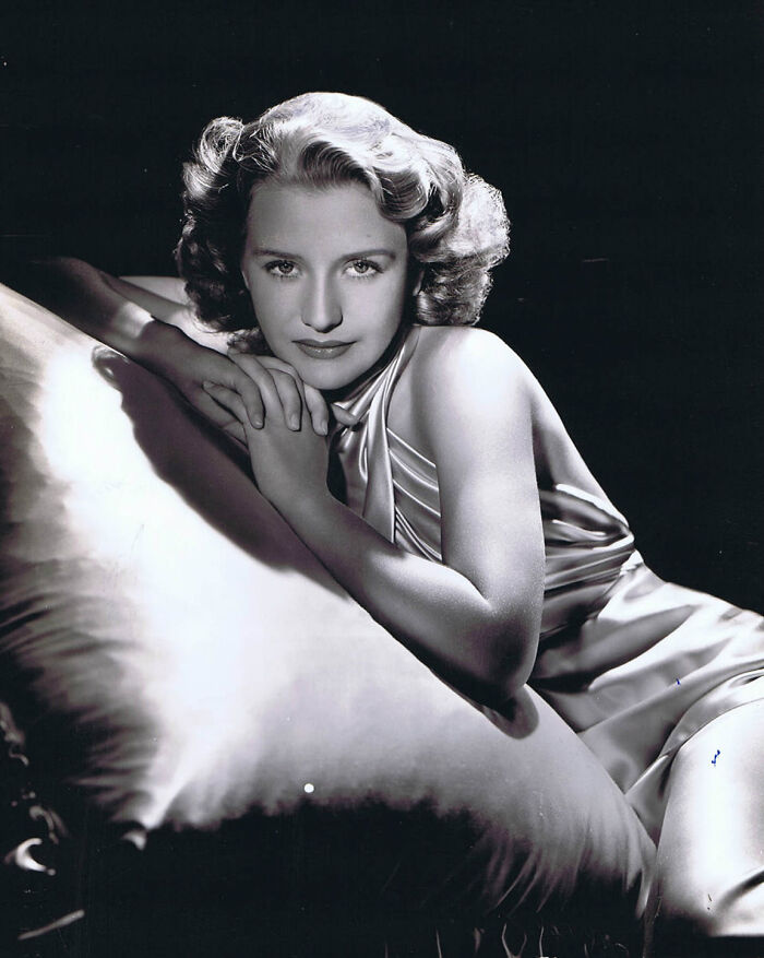 Black and white portrait of a glamorous 1940s icon reclining and posing in elegant vintage Hollywood style.