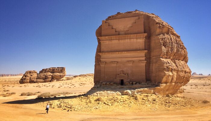 Ancient hidden UNESCO gem carved into sandstone rock in a vast desert landscape under clear blue sky.