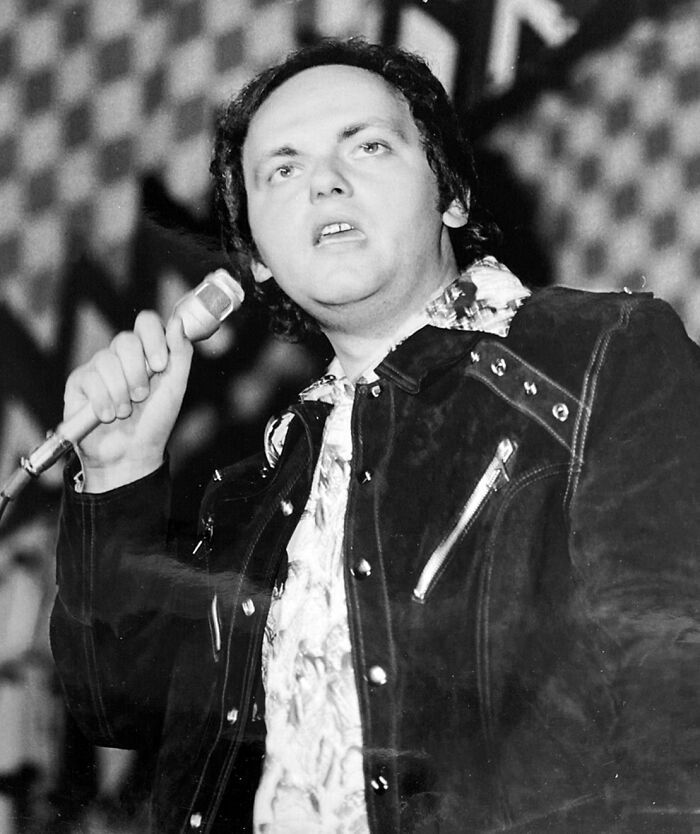 Black and white photo of a man holding a microphone performing, related to notable people who passed away in 2025.