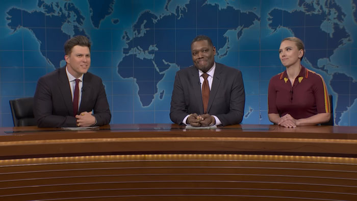 Scarlett Johansson and husband seated with co-hosts on SNL news desk, reacting to roast beef joke segment. Scarlett Johansson and husband seated with co-hosts on SNL news desk, reacting to roast beef joke segment.