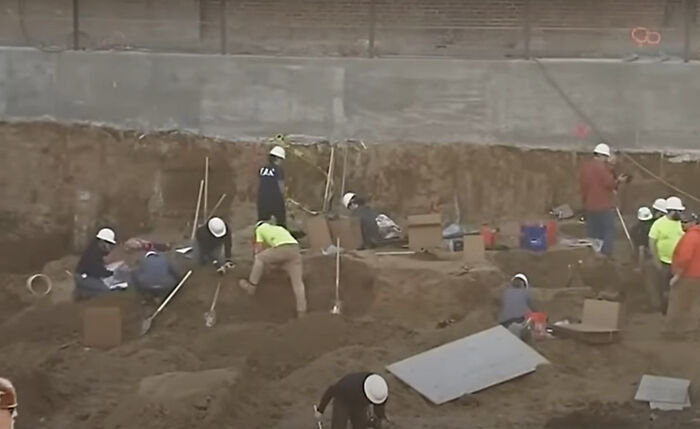 Archaeologists excavating a site carefully uncovering bizarre historical artifacts during an active dig with safety helmets on.
