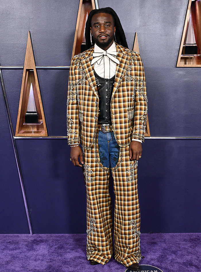 Man wearing an embellished plaid suit with wide-leg pants and a bow tie at an event, highlighting worst dressed stars keyword.