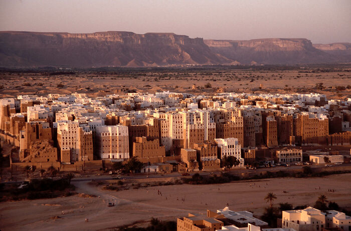 Ancient mudbrick buildings of a UNESCO treasure site set against a mountainous desert landscape at sunset.