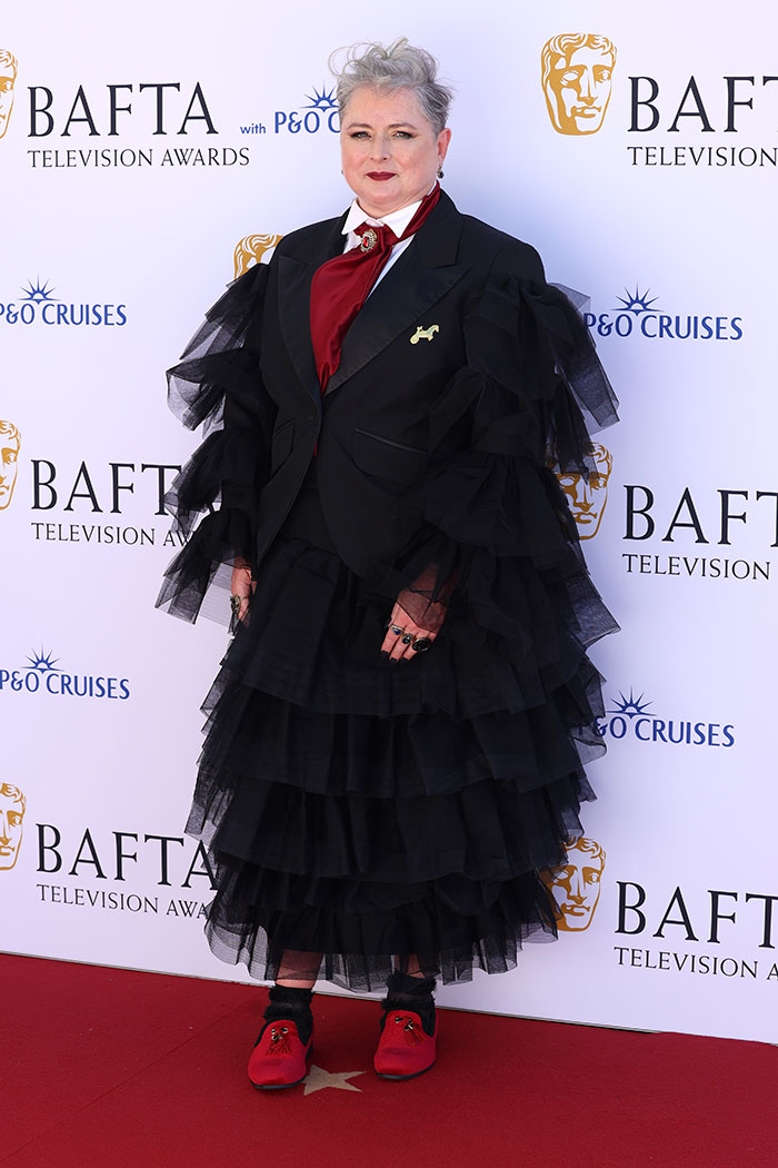 Person wearing a layered black ruffle dress with red shoes on the red carpet at the BAFTA TV Awards worst dressed stars.